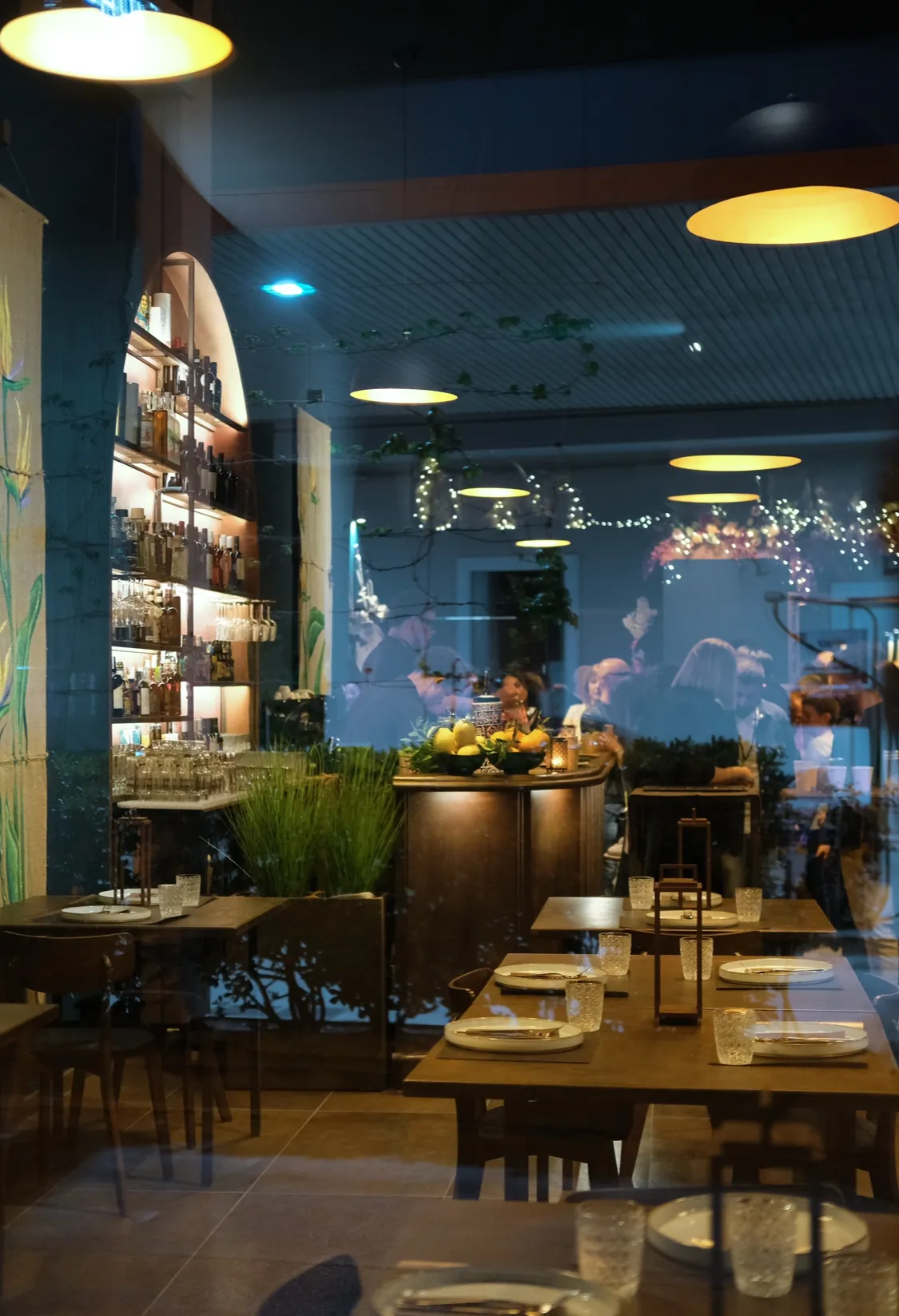 Sala del ristorante con pareti blu, tavoli apparecchiati e luci calde a sospensione.