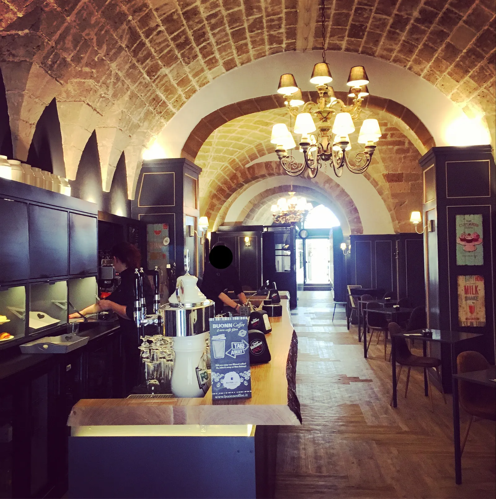 Sala con volte in pietra, lampadari classici, boiserie blu e bancone, vista in prospettiva.