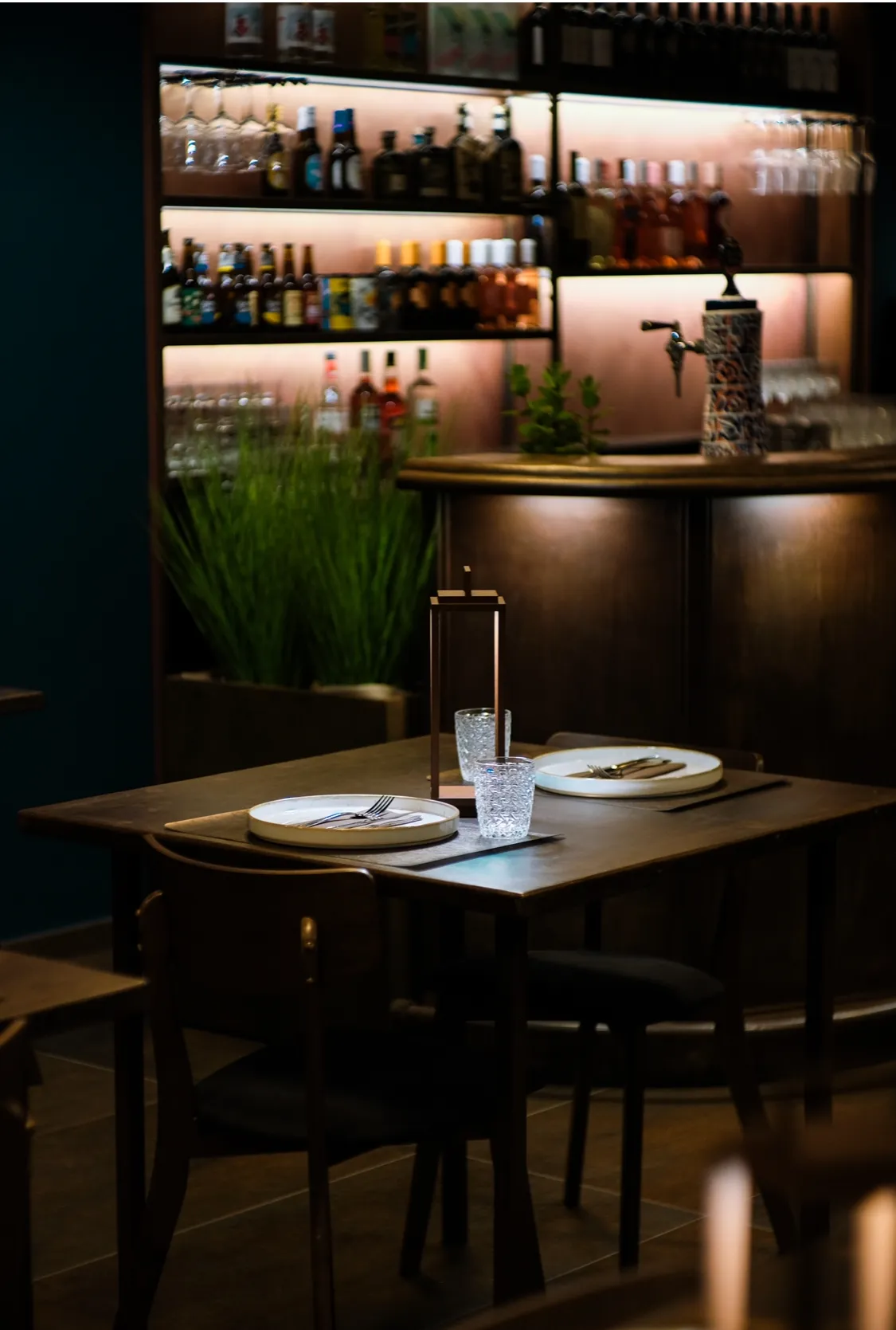 Tavolo per due apparecchiato davanti al banco bar illuminato.